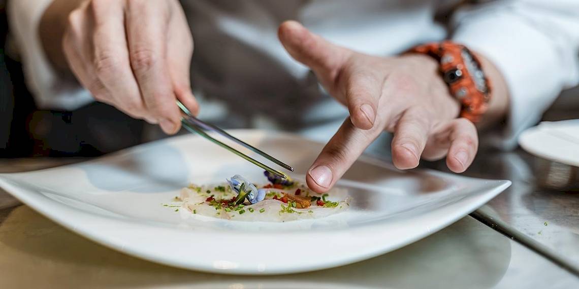 Koch in der Küche des Myconian Ambassador Relais & Chateaux, der ein Gericht auf einem Teller dekoriert
