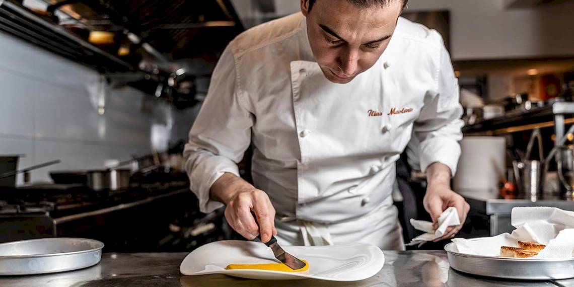 Koch im Myconian Ambassador Hotel bereitet ein Gericht auf einem Teller zu.