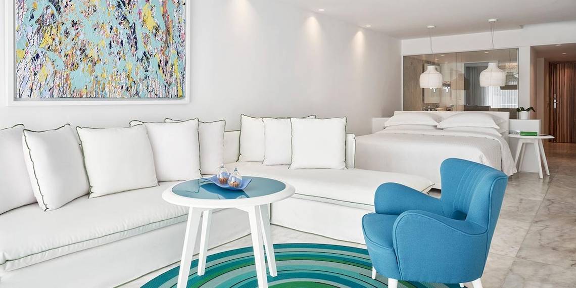 Suite-Innenbereich im Myconian Ambassador Relais & Chateaux Hotel mit weißen Möbeln und einem modernen Kunstwerk.