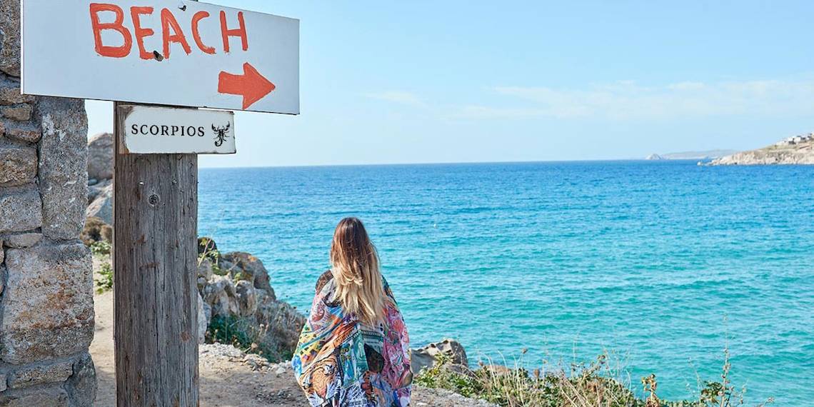 Frau steht am Strand vor einem Schild mit der Aufschrift Beach und einem Pfeil, der auf das Meer zeigt.