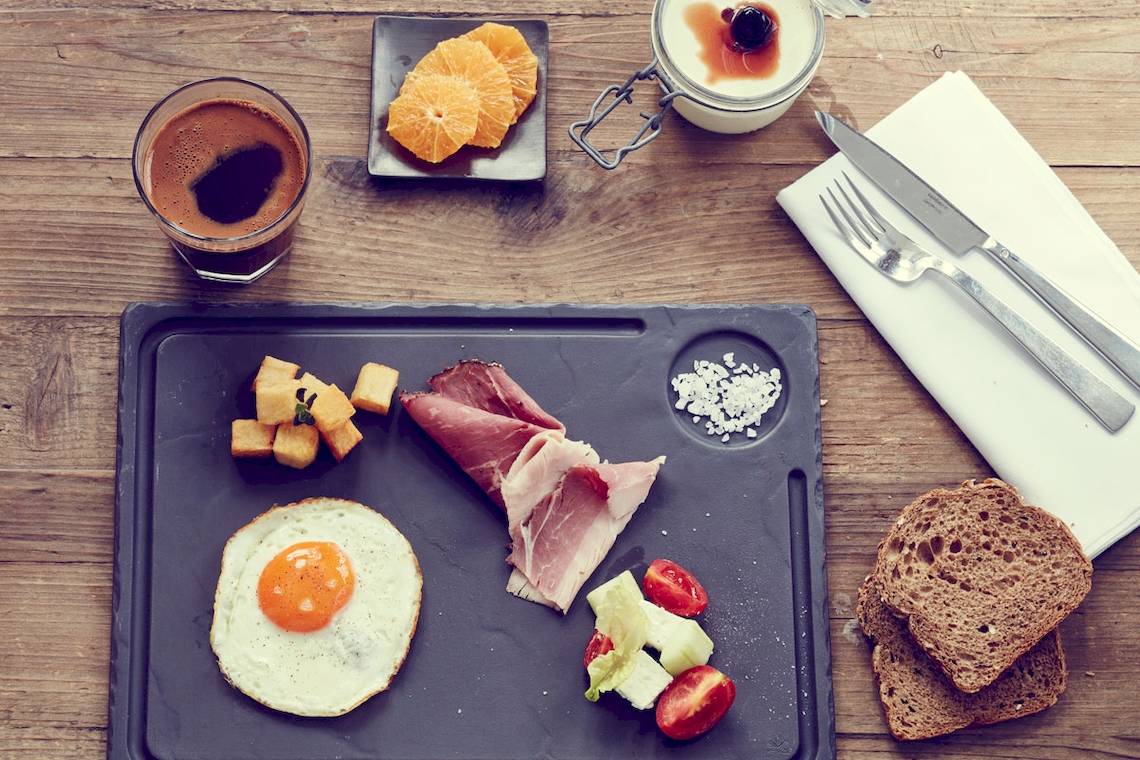 Frühstücksplatte im Myconian Ambassador Hotel mit Ei, Schinken und Orangen.