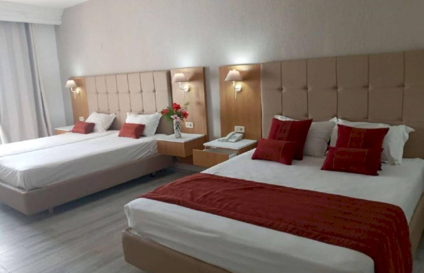 Zwei Doppelbetten in einem Hotelzimmer im Djerba Holiday Beach Hotel, jedes mit roten Kopfkissen und weißen Laken.