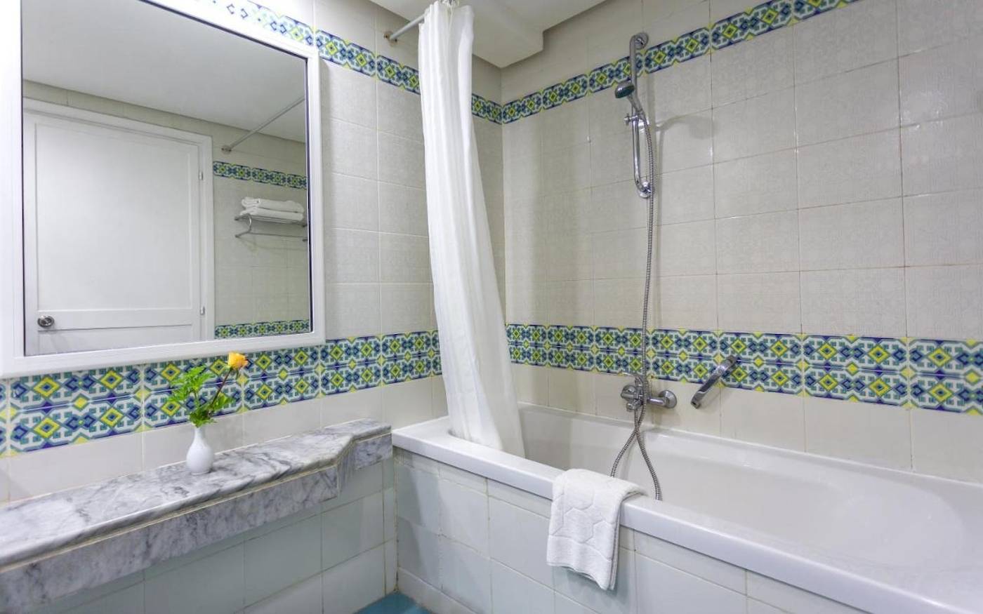 Badezimmer des Djerba Holiday Beach Hotels mit Badewanne, Dusche, Spiegel und Blumenvase.