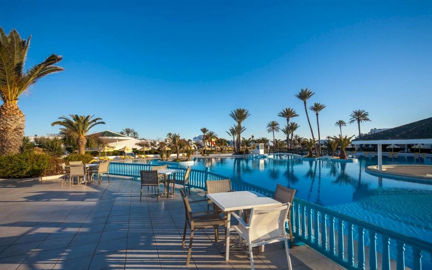 Außenpool des Djerba Holiday Beach Hotels mit umliegenden Tischen und Palmen