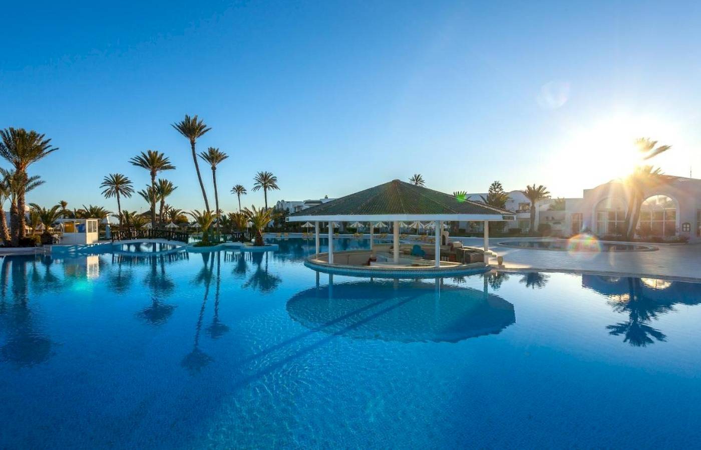 Außenpool des Djerba Holiday Beach Hotels mit Sonnenuntergang im Hintergrund.