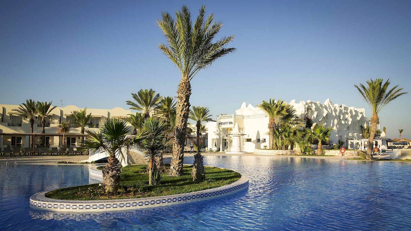 Außenansicht des Djerba Holiday Beach Hotels mit Pool, weißen Gebäuden und Palmen.