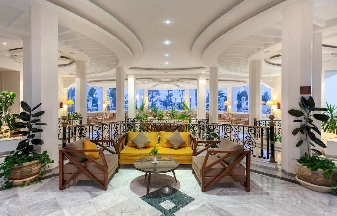 Lobby des Djerba Holiday Beach Hotels mit gelber Couch, Tischen und Pflanzen.