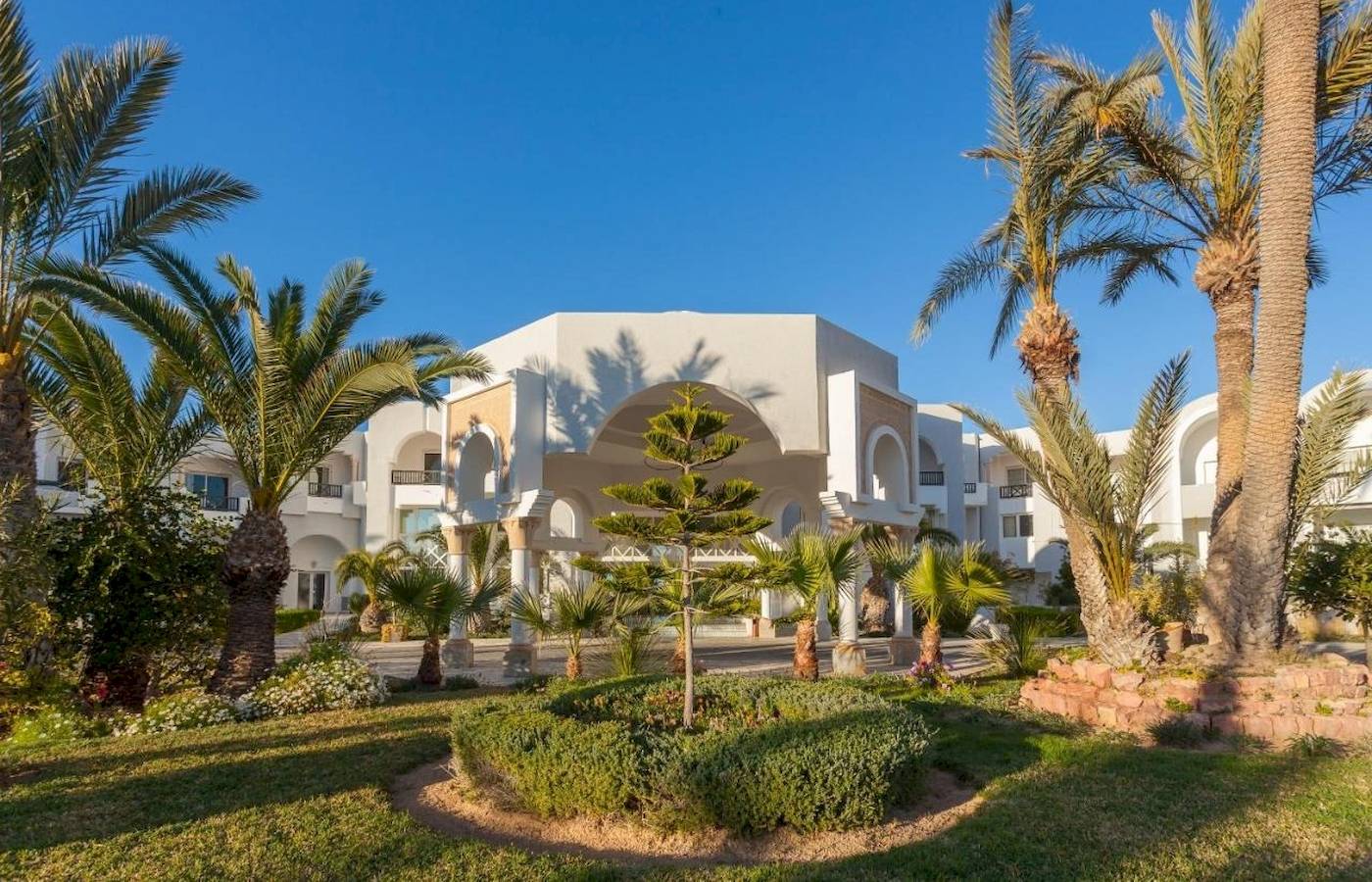 Vorne des Djerba Holiday Beach Hotels mit Palmen und Gebäuden im Hintergrund