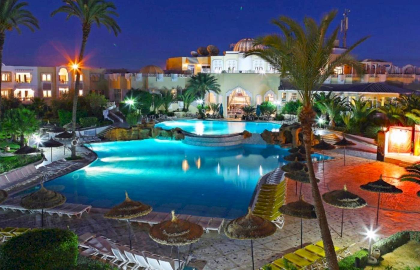 Abendliche Ansicht des Djerba Holiday Beach Hotels mit Swimmingpool und Palmen.