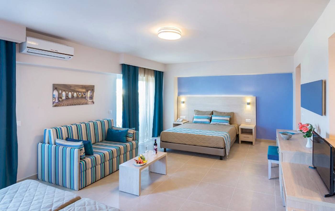 Inneneinrichtung eines Zimmers im Irene Palace Beach Resort mit einem Doppelbett, einer Couch, einem Tisch und einer Klimaanlage.