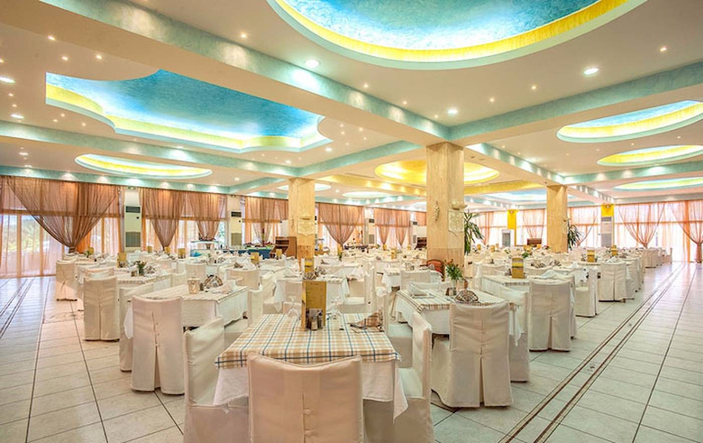 Ein großes geräumiges Restaurant im Irene Palace Beach Resort mit vielen gedeckten Tischen.