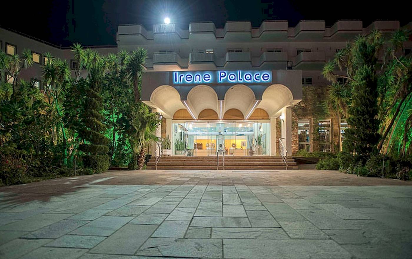 Außenansicht des Irene Palace Beach Resorts bei Nacht mit Beleuchtung und Pflanzen davor.