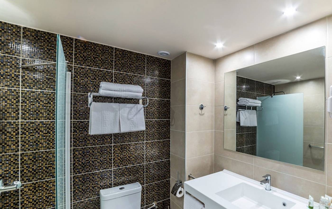 Badezimmer im Irene Palace Beach Resort mit gefliester Wand, Glasdusche und Spiegel.