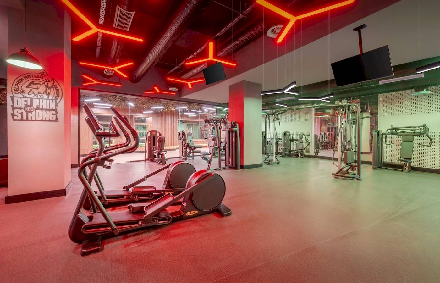 Innenansicht des Fitnesscenters im Delphin Palace Hotel mit roter Beleuchtung und Fitnessgeräten.