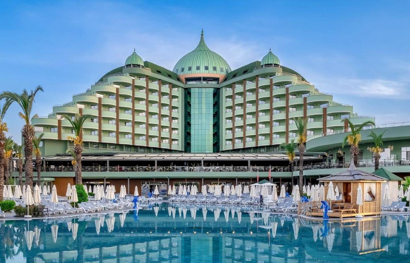 Außenansicht des Delphin Palace Hotels mit großen grünen Kuppeln, Swimmingpool und vielen Liegestühlen.