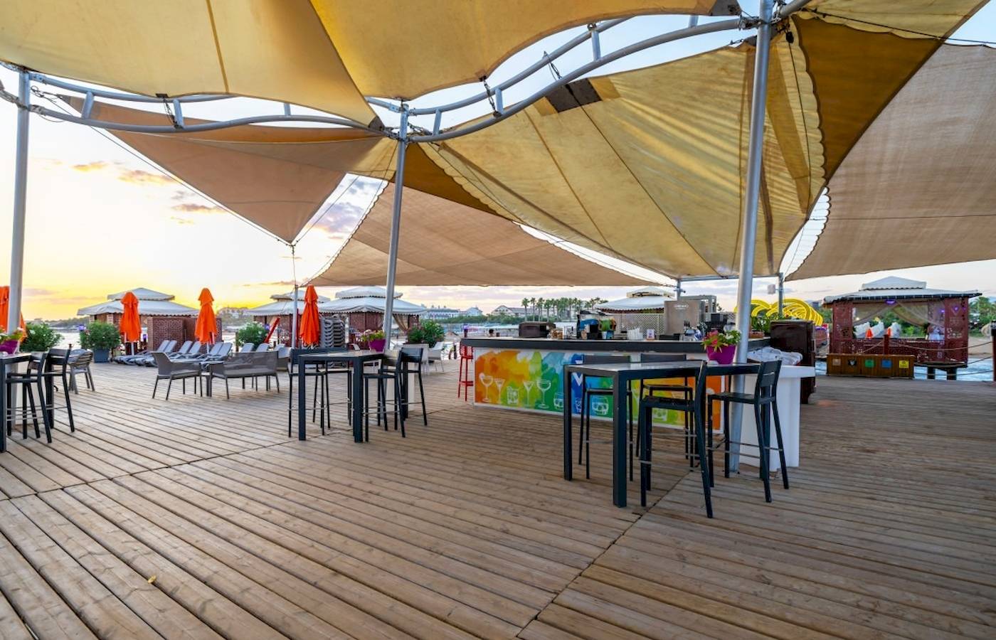 Terrasse des VONRESORT Golden Coast mit Tischen, Stühlen und Sonnenschirmen bei Sonnenuntergang.