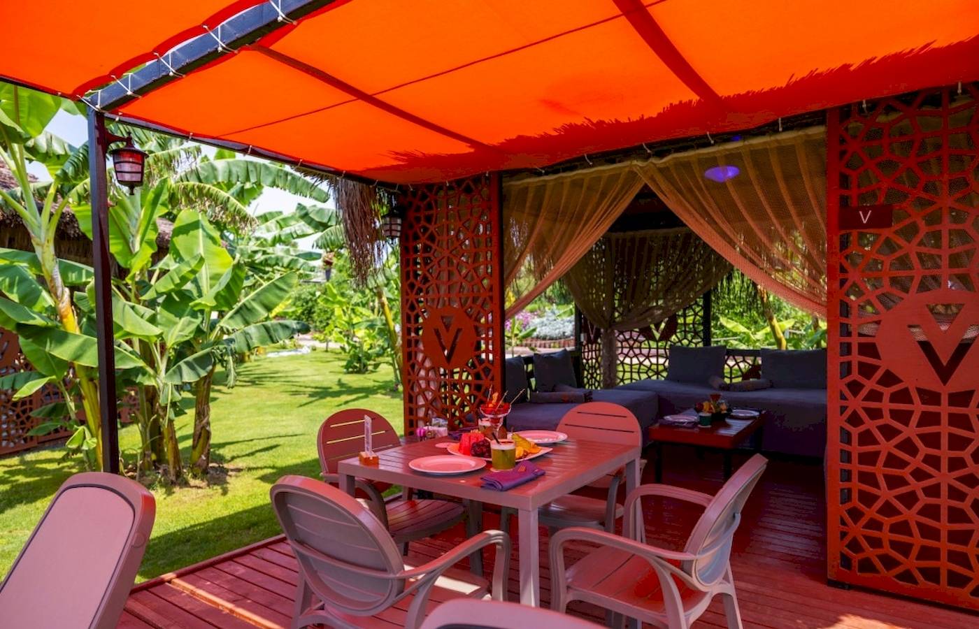 Sitzecke im Freien des VONRESORT Golden Coast mit rotem Sonnendach und grüner Wiese.
