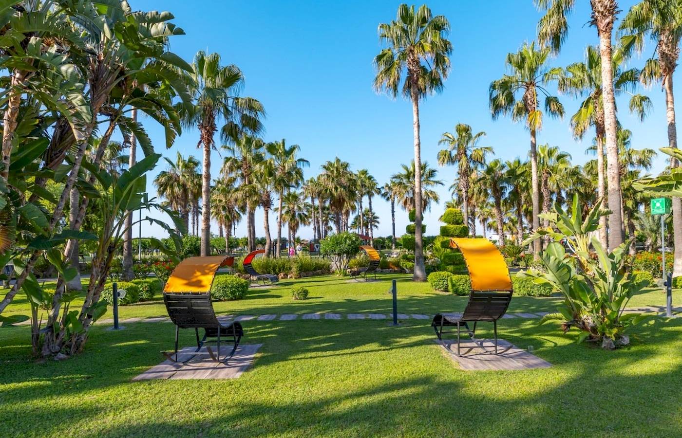 Gartenlandschaft des VONRESORT Golden Coast mit gelben Liegestühlen und Palmen