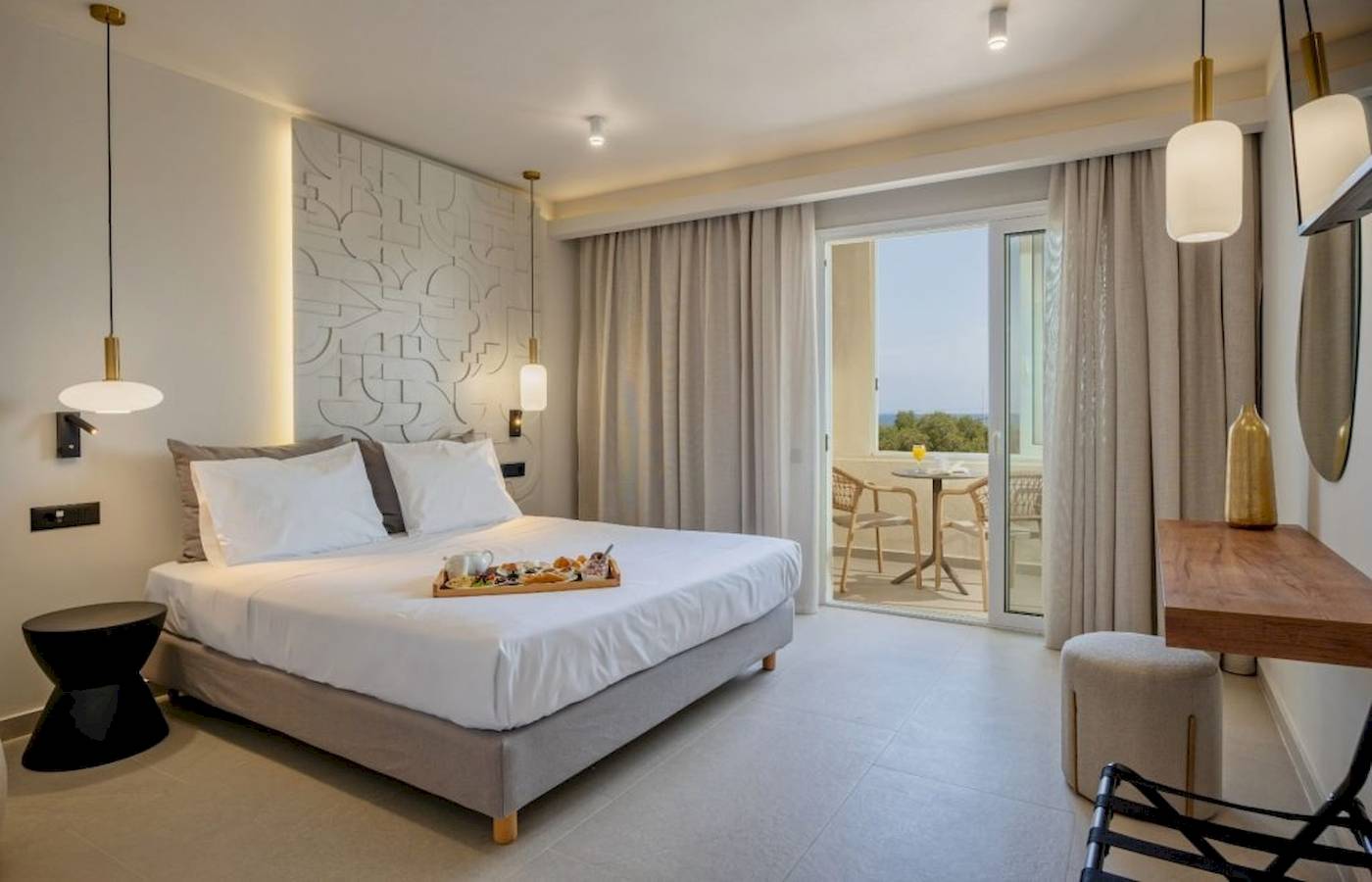 Innenansicht eines Hotelzimmers im Georgioupolis Resort Aquapark & SPA mit Bett, Frühstückstablett, Tisch und Balkon.