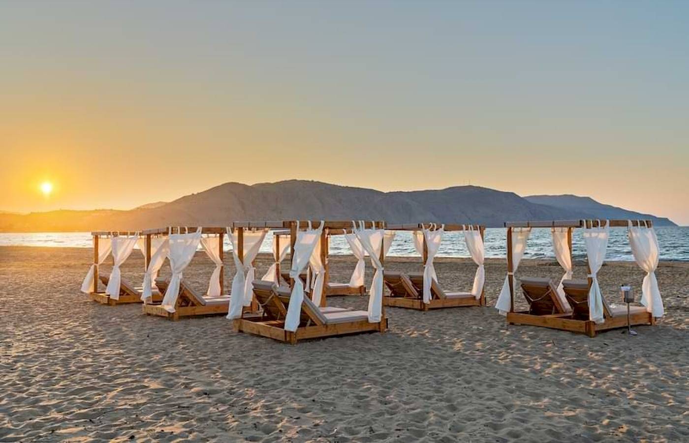Georgioupolis Resort Aquapark & SPA mit Sonnenuntergang am Strand mit weißen Sonnenschirmen
