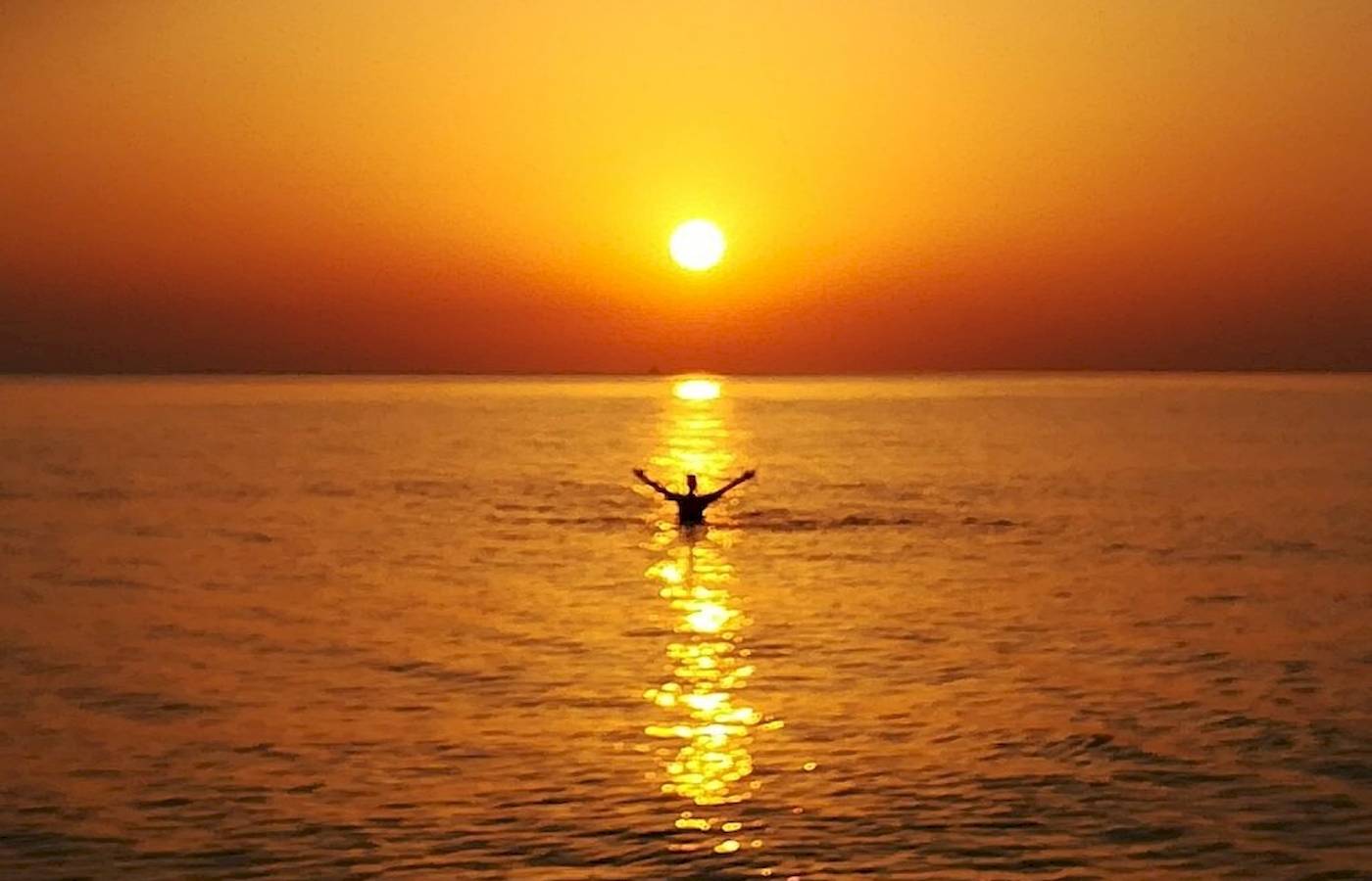 Eine Person schwimmt im Meer während des Sonnenuntergangs, mit der Sonne, die auf dem Horizont untergeht.