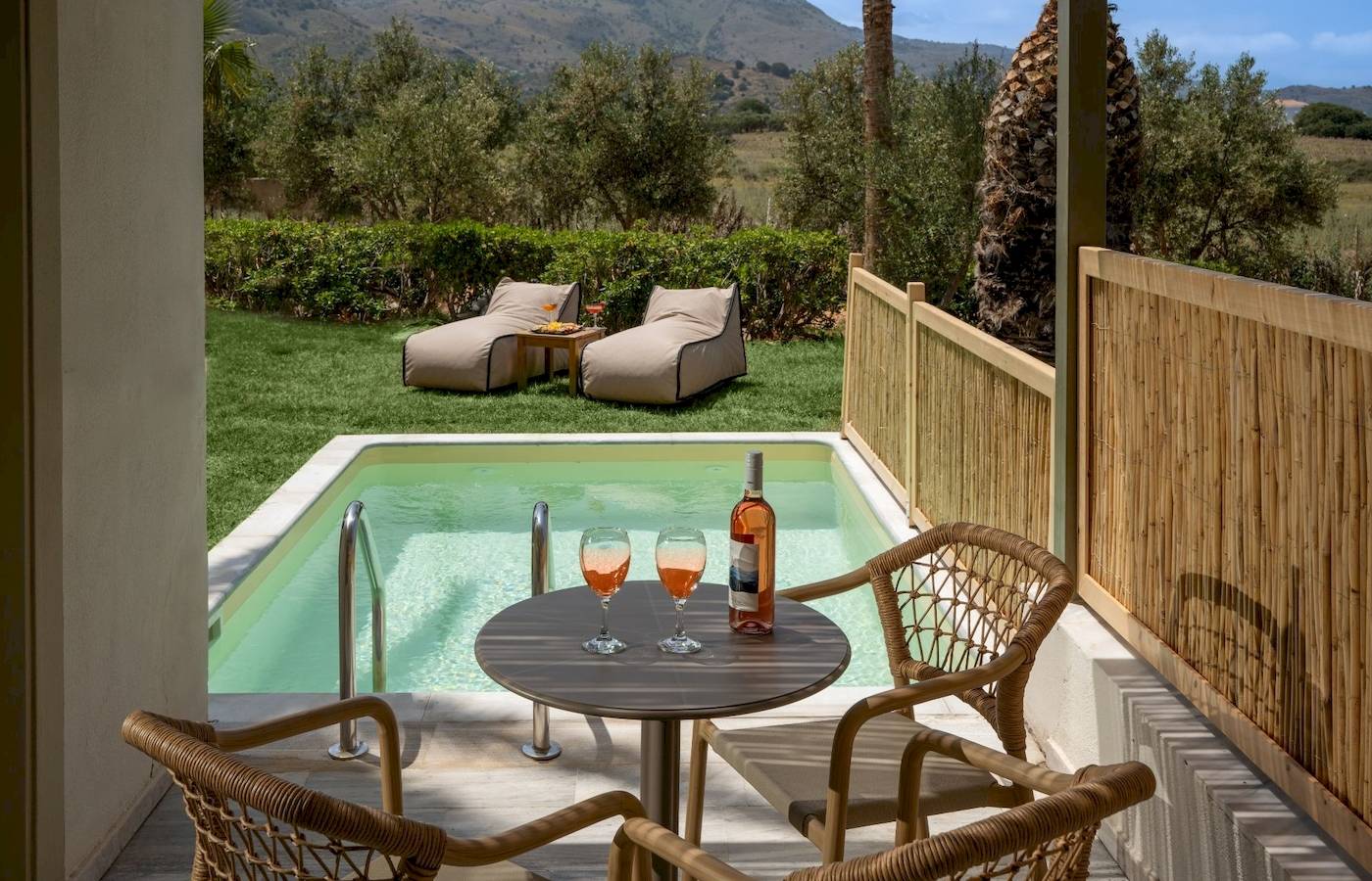 Terrasse im Georgioupolis Resort Aquapark & SPA mit Blick auf einen Swimmingpool, Liegen und Weinflasche.