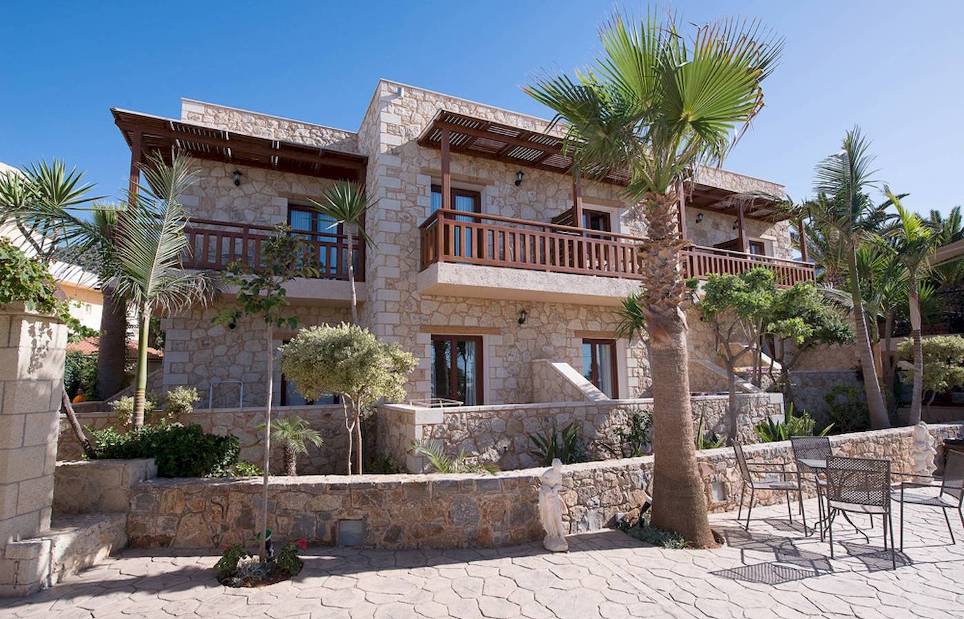 Außenansicht des Cactus Village Hotel & Bungalows mit Steinmauer und Palmen.