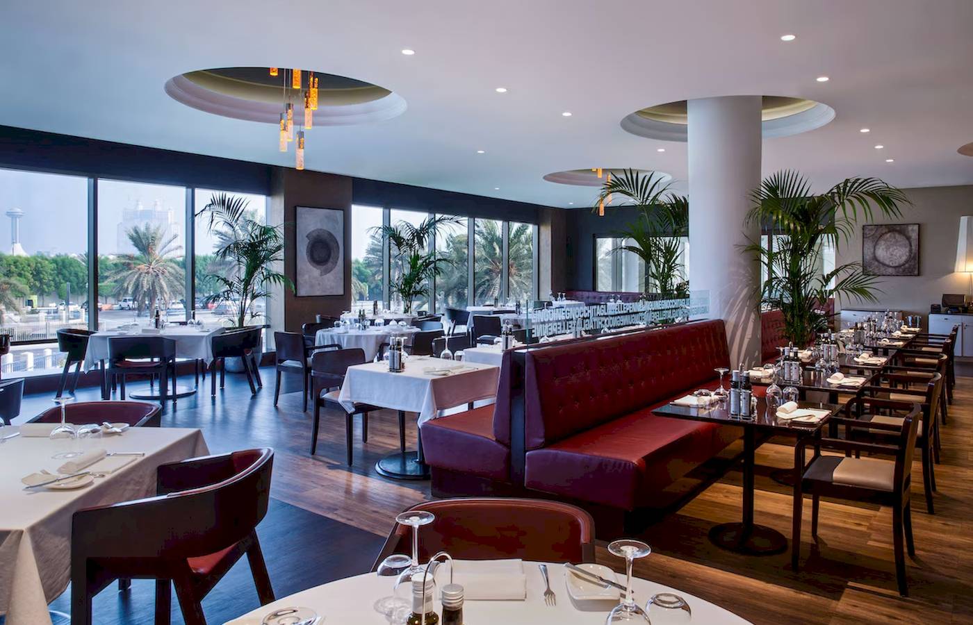 Innenansicht des Restaurants des Radisson Blu Hotel & Resort, Abu Dhabi Corniche mit runden Tischen und roten Sitzbänken.