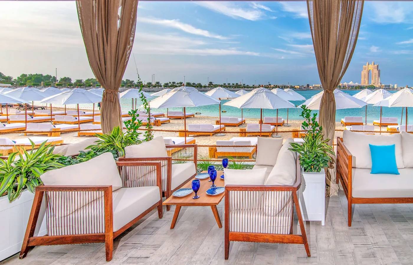 Außenbereich des Radisson Blu Hotel & Resort in Abu Dhabi mit weißen Sonnenschirmen und Möbeln am Strand.