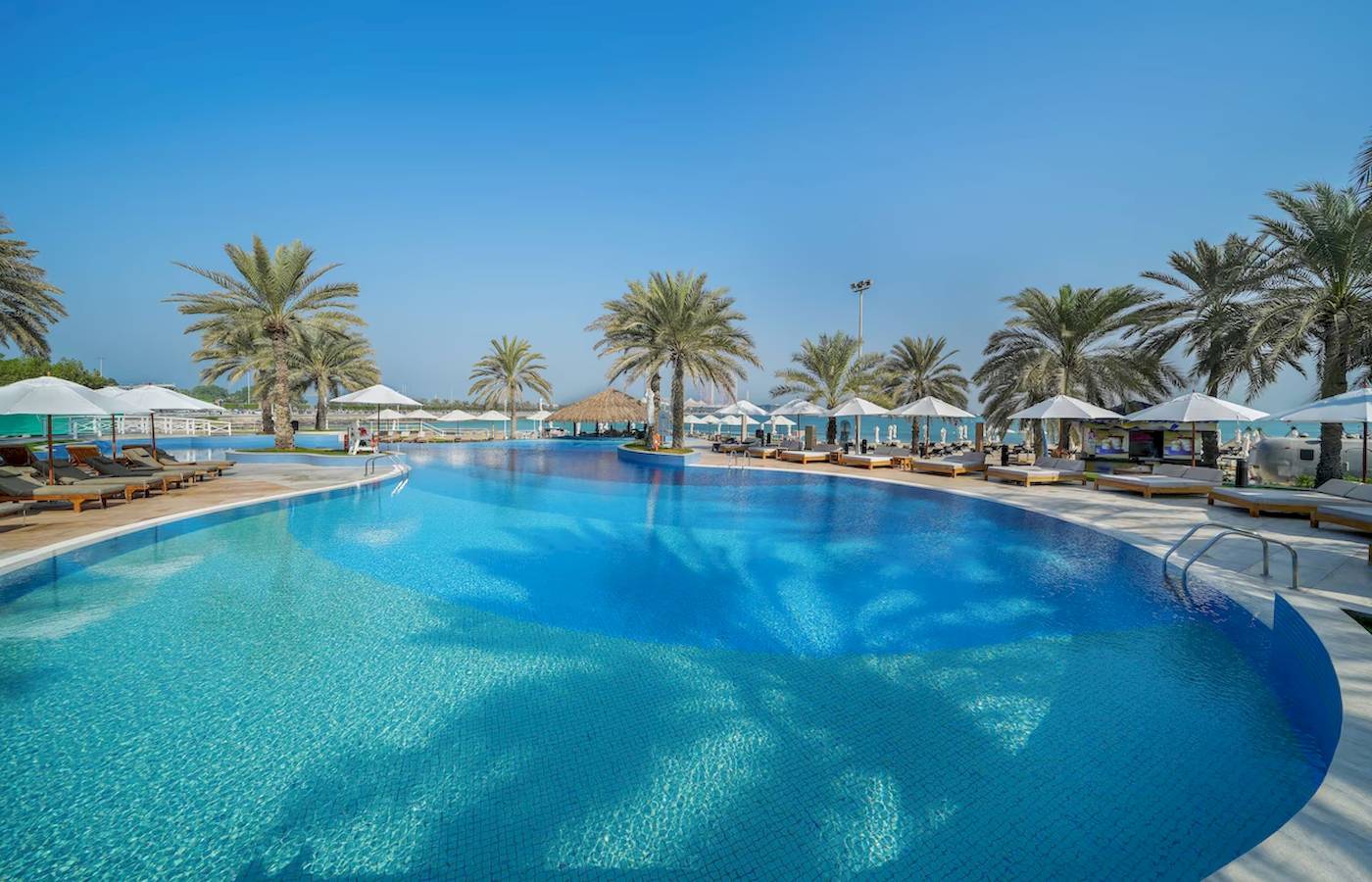 Außenpool im Radisson Blu Hotel & Resort, Abu Dhabi Corniche, umgeben von Liegestühlen und Sonnenschirmen.