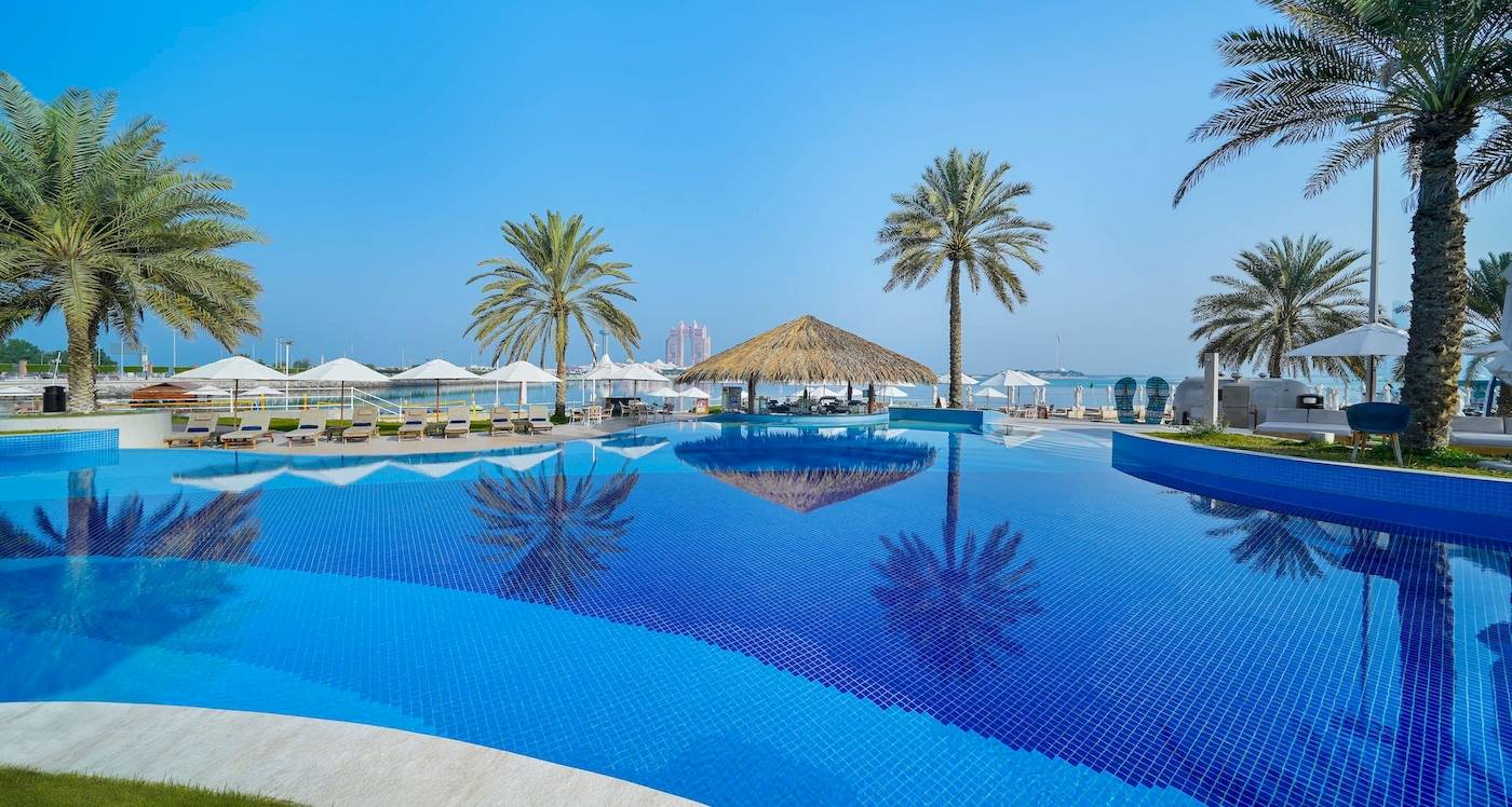 Poolbereich des Radisson Blu Hotel & Resort am Abu Dhabi Corniche mit Sonnenliegen und Palmen
