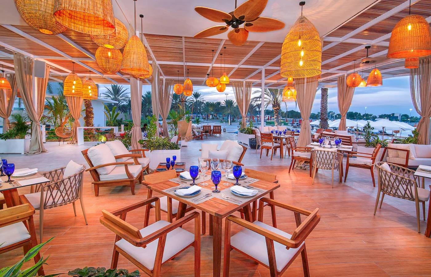 Innenbereich des Restaurants im Radisson Blu Hotel & Resort, Abu Dhabi Corniche, mit hängenden Lampen und gedeckten Tischen.