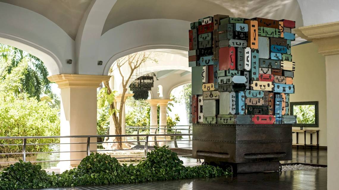 Eingangsbereich des Hotels JOIA Bávaro by Iberostar mit einer großen, bunten Koffer-Skulptur.