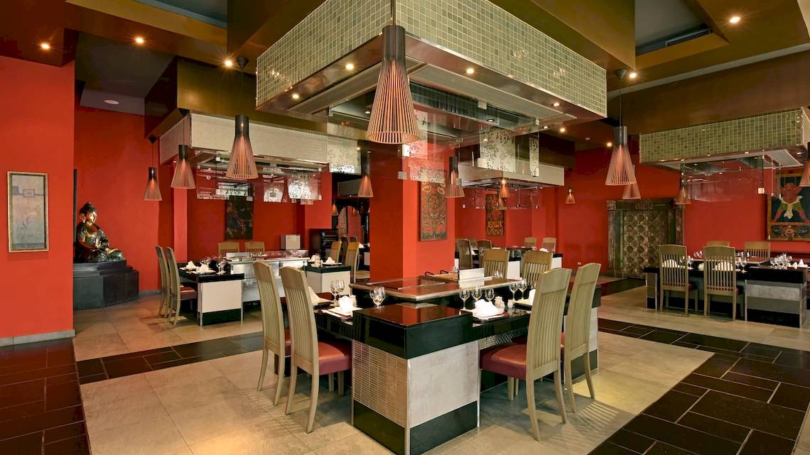 Innenbereich des Restaurants im Iberostar Grand Bavaro Hotel mit roten Wänden, modernen Möbeln und einer Buddha-Statue.