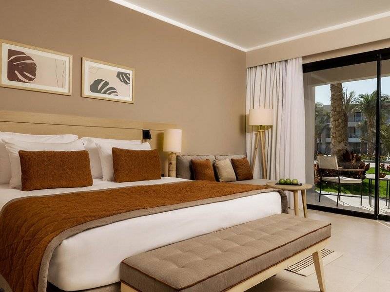 Ein Schlafzimmer mit einem Bett, Kissen, einem Couch, einem Tisch und einer Terrasse im Jaz Elite Amara Hotel