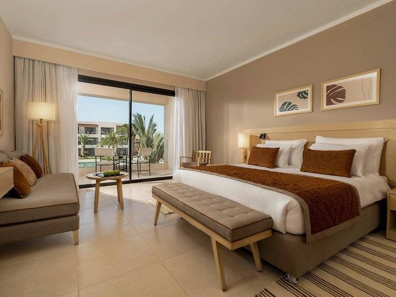 Suite-Zimmer im Jaz Elite Amara Hotel mit großem Bett und Aussicht auf den Pool.