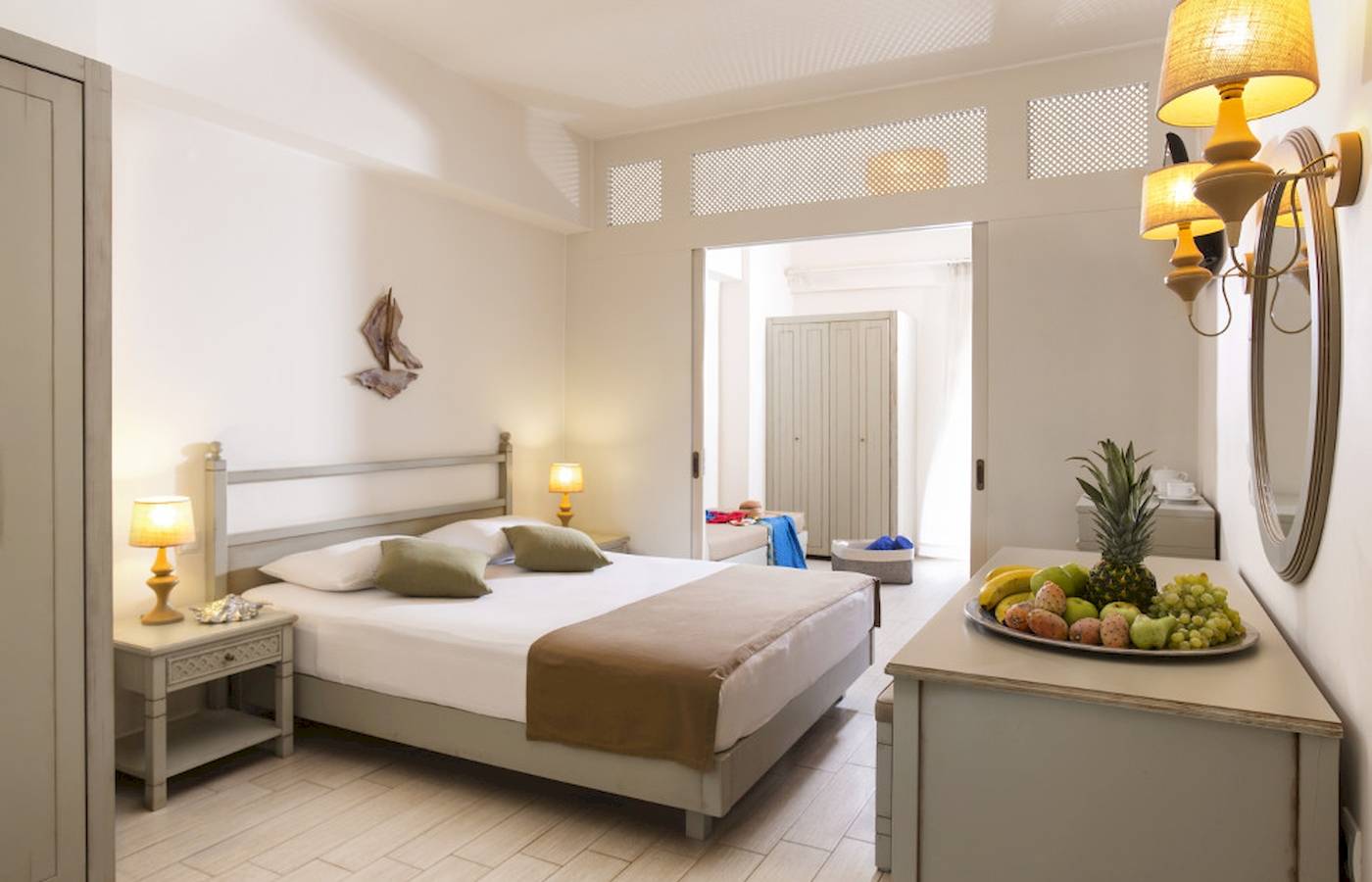 Innenansicht eines Zimmers im Almyrida Beach Hotel mit einem Bett, Nachttischen und Früchten auf einem Tisch.