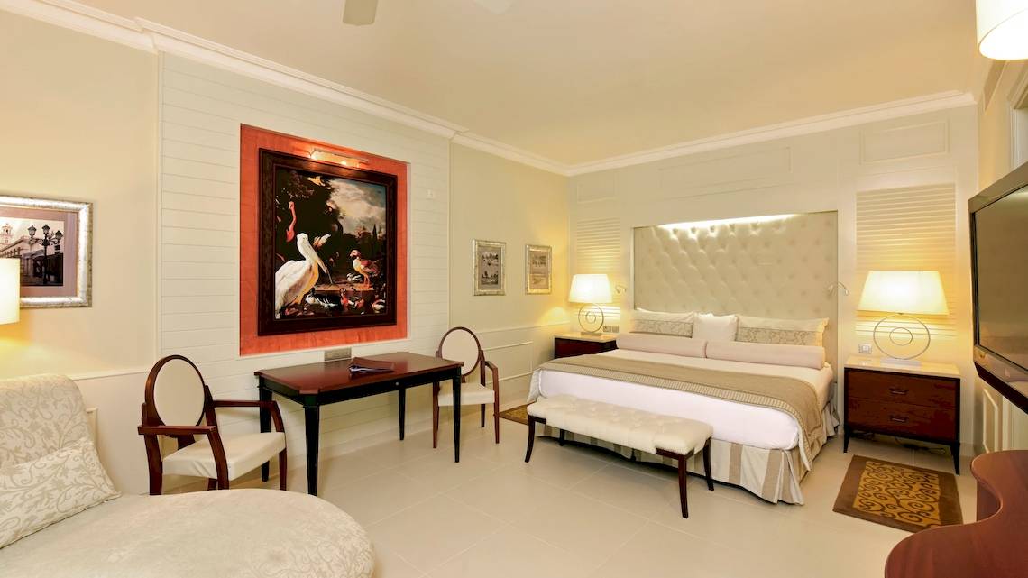 Suite-Schlafzimmer im JOIA Bávaro by Iberostar mit Doppelbett, Schreibtisch und Stühle.