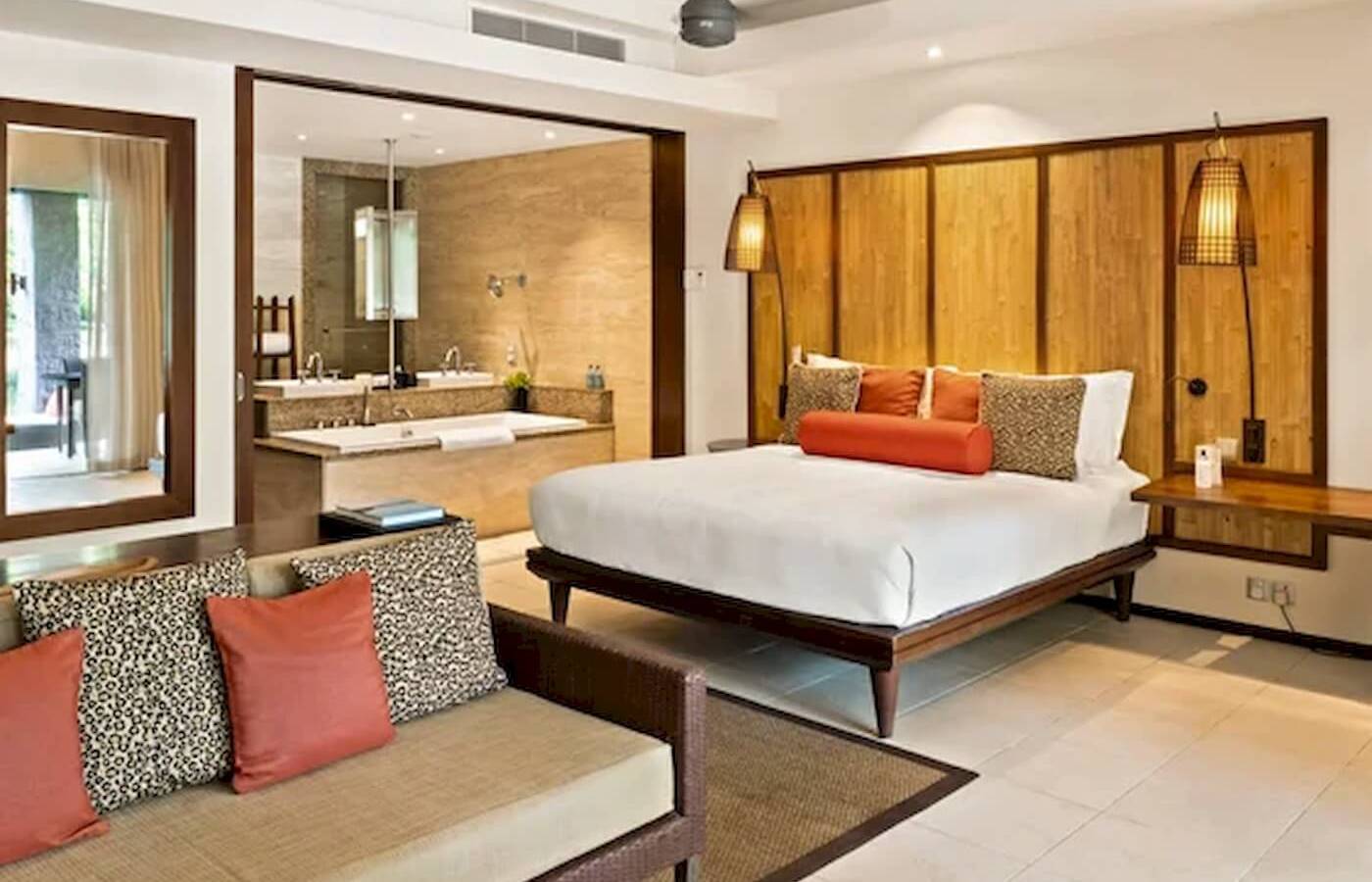 Innenansicht eines Schlafzimmers im Constance Ephelia Resort mit großem Bett, Sofa, Badewanne und Dekor.