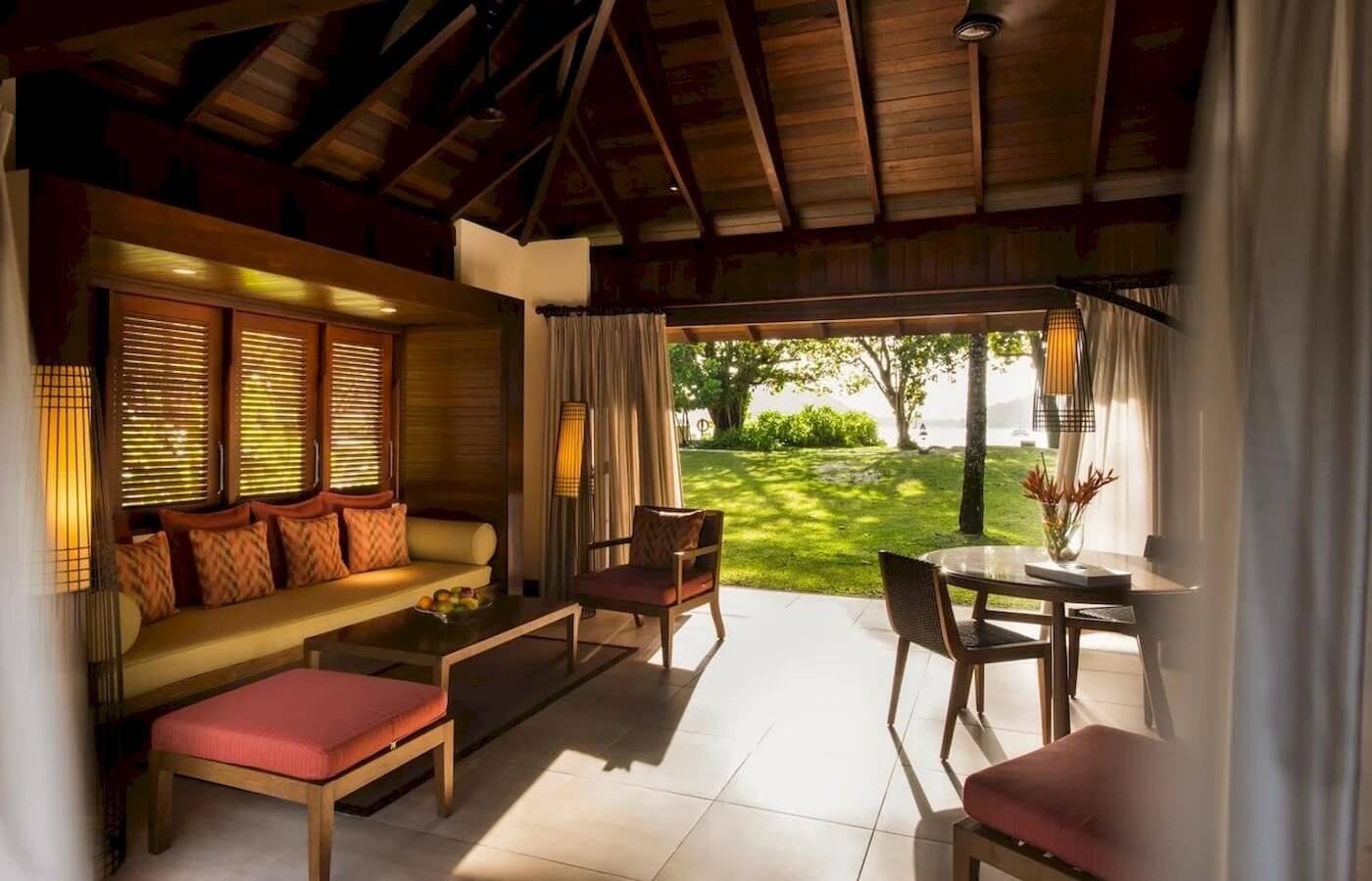 Innenansicht des Wohnbereichs im Constance Ephelia Resort mit Couch, Tisch, Stühlen und Ausblick auf Rasen.