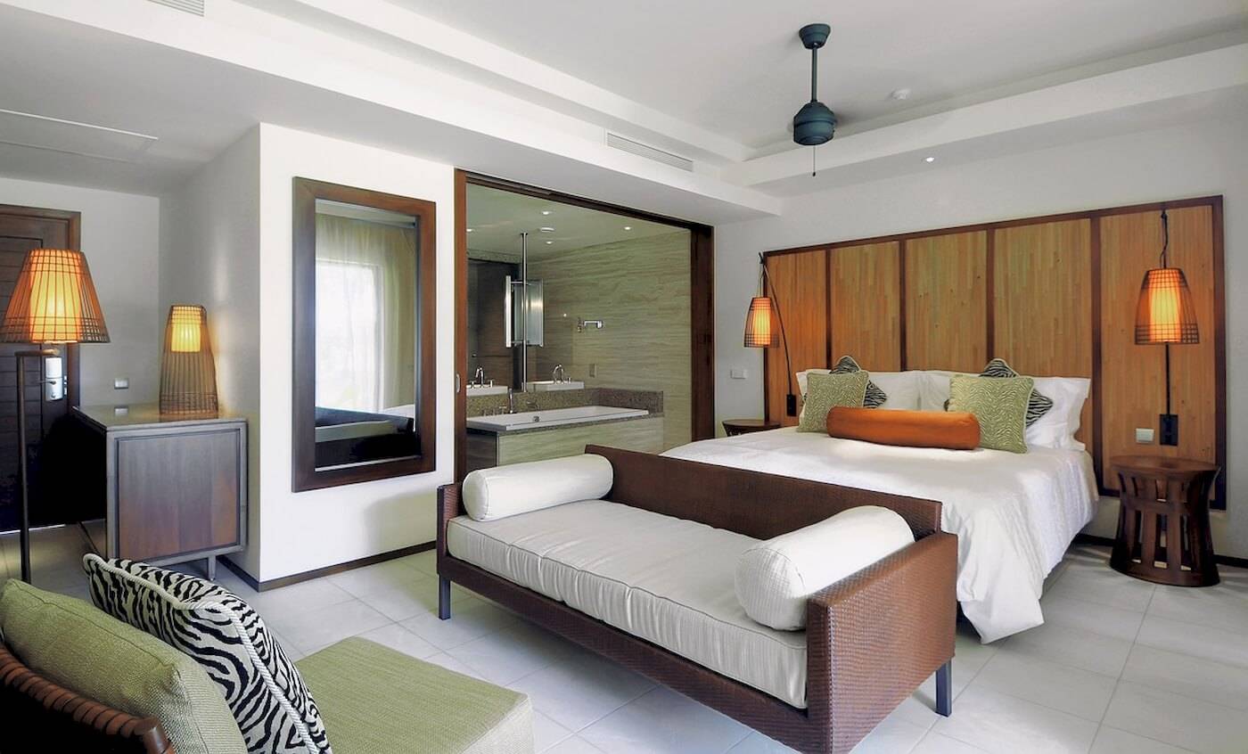 Innenansicht des Schlafzimmers im Constance Ephelia Resort mit Bett, Sofa, Spiegeln und Lampen.