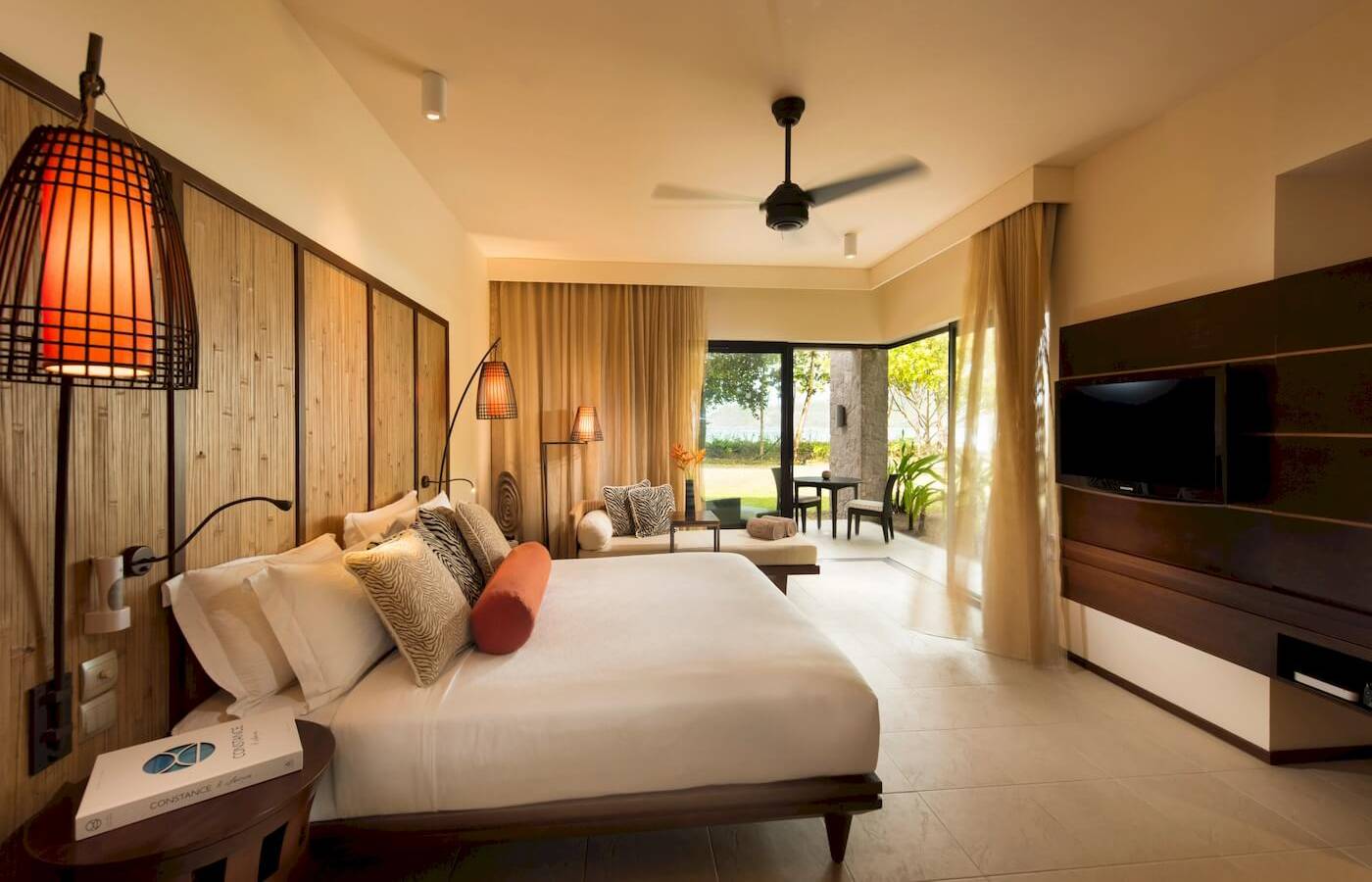 Luxuriöses Schlafzimmer im Constance Ephelia Resort mit Bett, Sofa, Tisch und Fernseher.