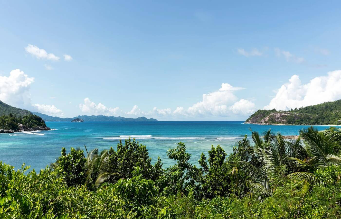 Aussicht auf das Meer vom Constance Ephelia Resort aus, mit blauem Himmel, Wellen und grünen Pflanzen.
