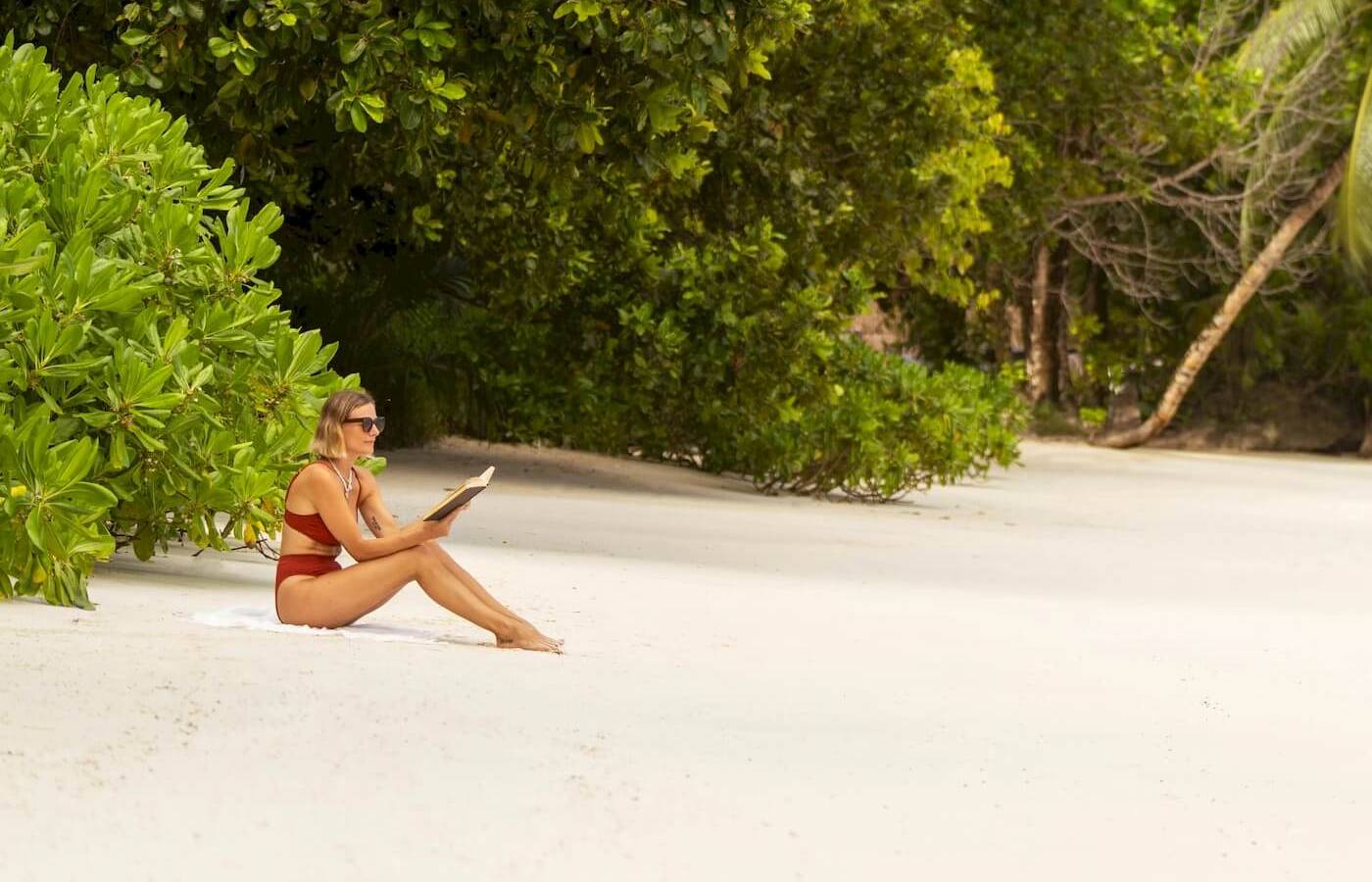 Frau sitzt am Strand im Constance Ephelia Resort und liest ein Buch.