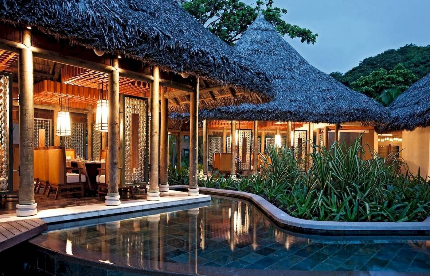 Außenbereich des Constance Ephelia Resorts mit Swimmingpool und traditionellen Strohdächern