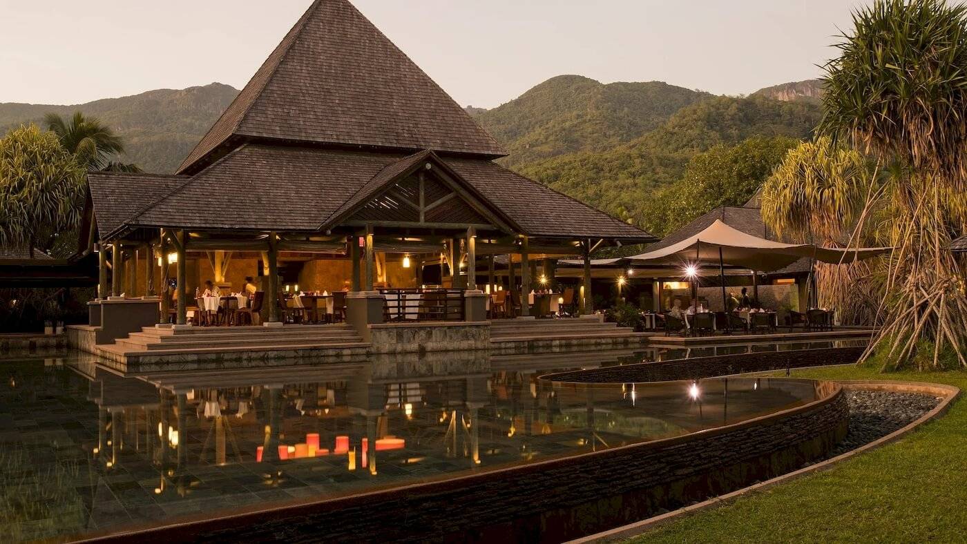 Außenansicht des Constance Ephelia Resorts mit Swimmingpool und Bergpanorama im Hintergrund.