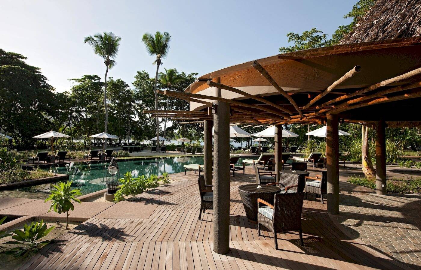 Terrasse im Constance Ephelia Resort mit Tischen, Stühlen und Sonnenschirmen am Swimmingpool.