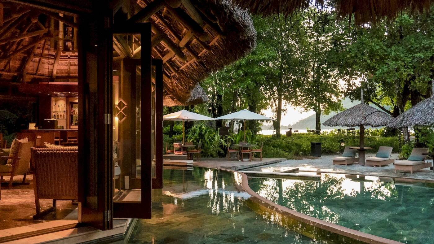 Außenbereich des Constance Ephelia Resorts mit Pool, Sonnenschirmen und Loungemöbeln.