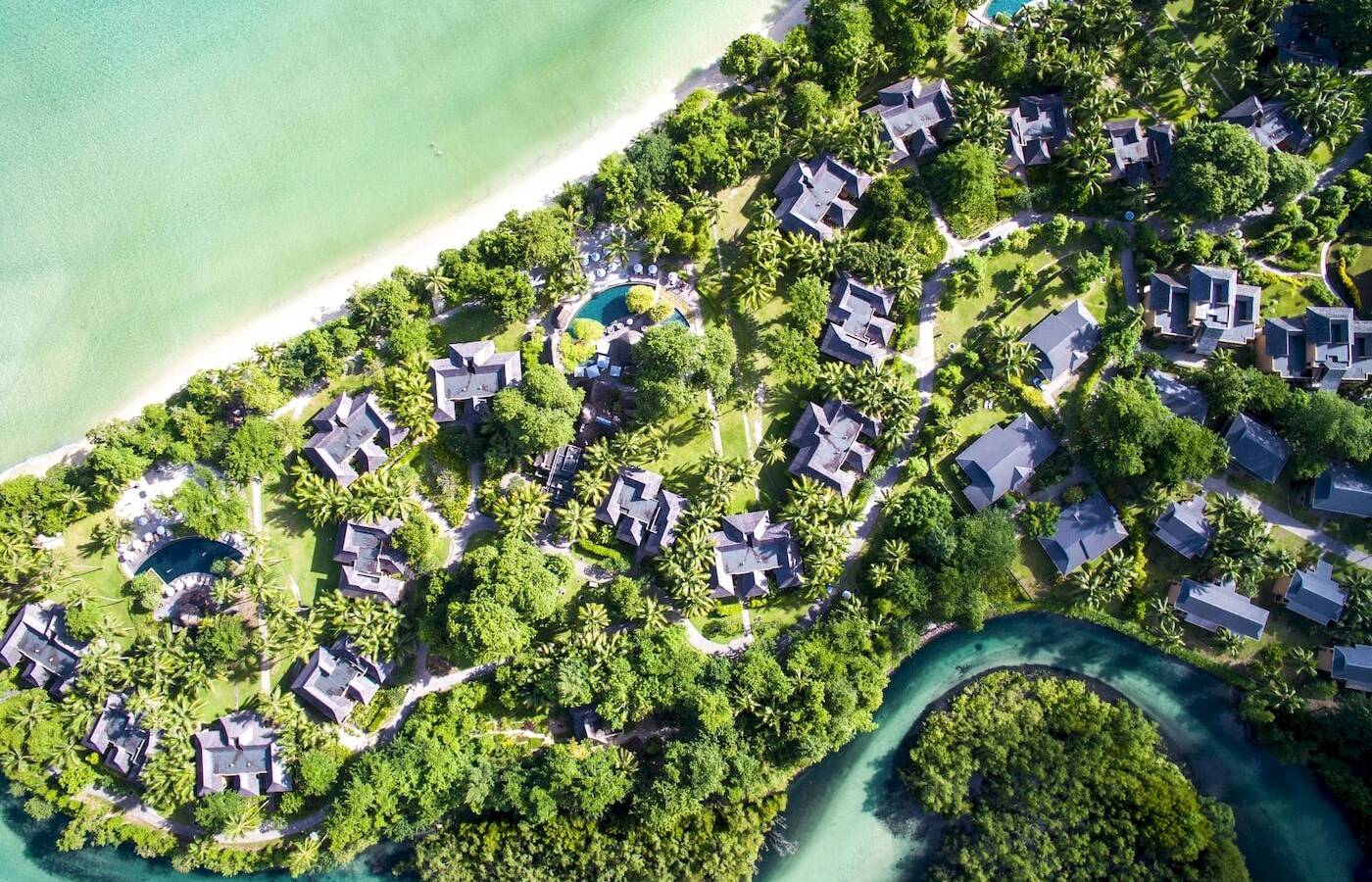 Aussenansicht des Constance Ephelia Resorts mit vielen kleinen Häusern, Pools und einem Fluss