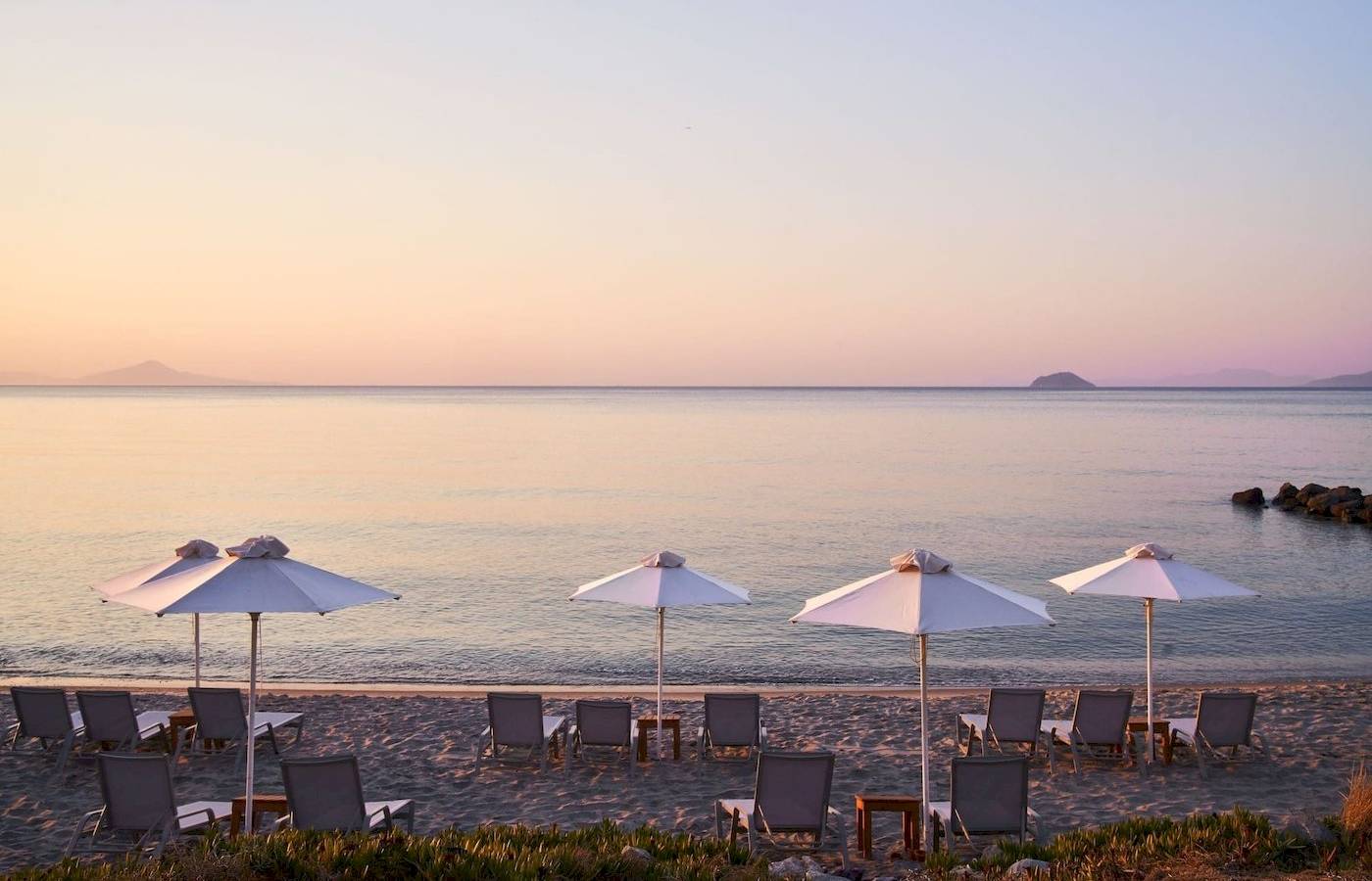 Sonnenuntergang am Strand des Atlantica Beach Resort Kos mit Sonnenschirmen und Liegen